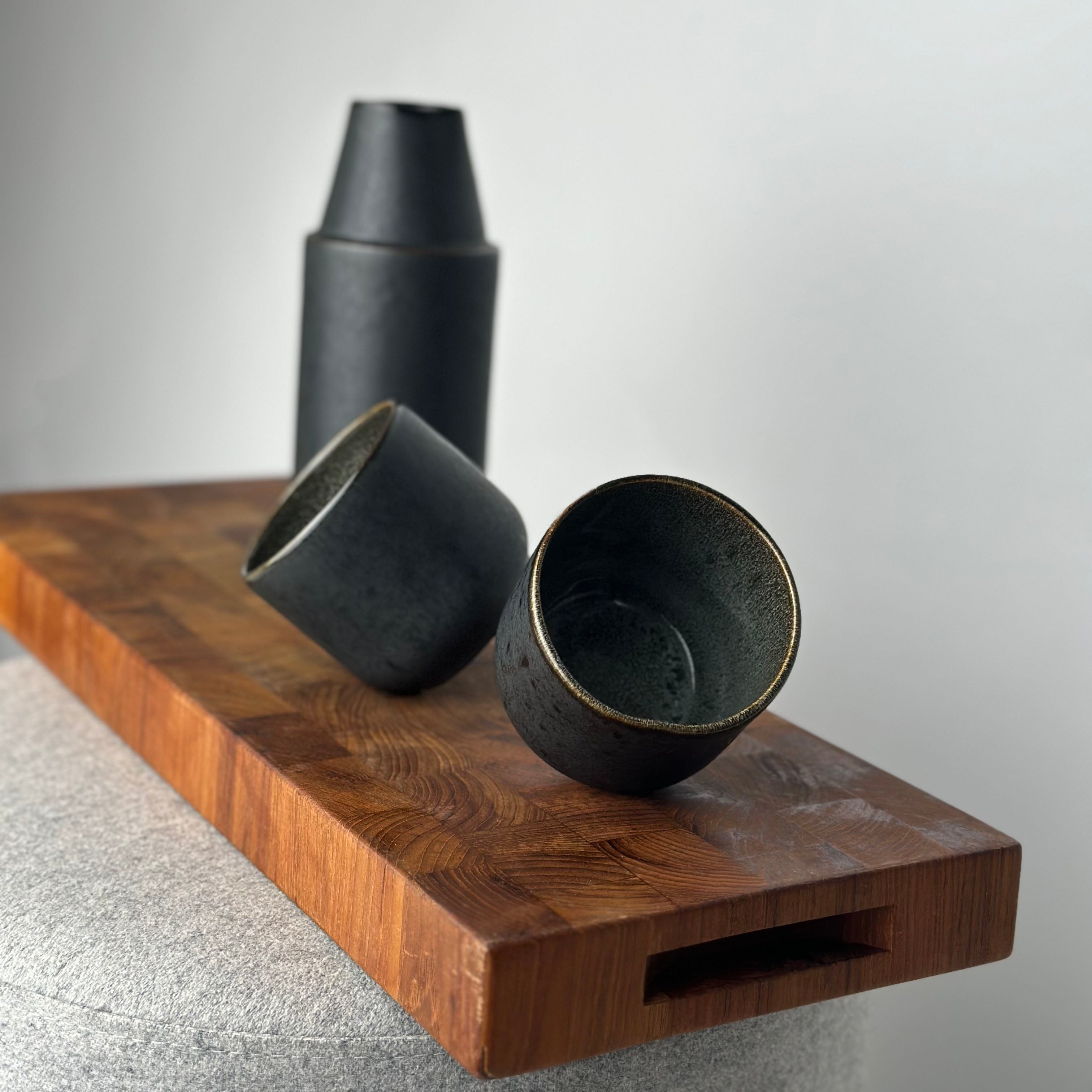 Handegemachte Karaffe und Becher auf Holzbrett in schwarz