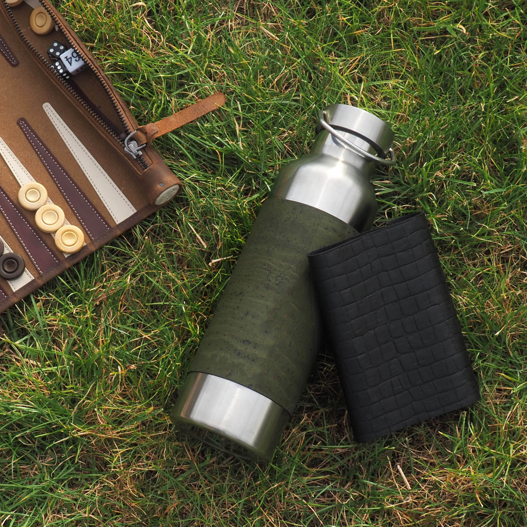 Edelstahltrinkflasche mit Grünen und schwarzem Korksleeve liegend im Gras