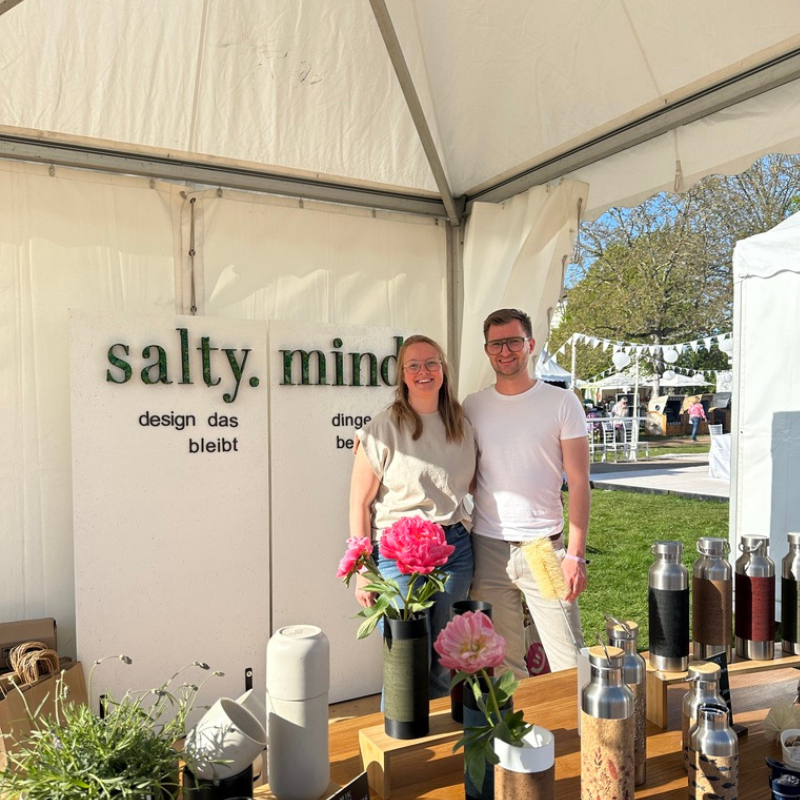 Zwei Personen am Messestand mit Vasen, Blumen und Trinkflaschen — Salty Mind